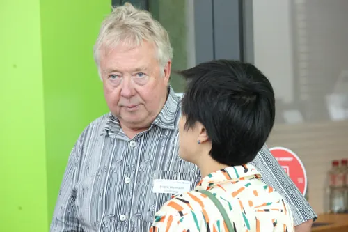 Zwei Teilnehmende im Gespräch vor grüner Wand im Foyer.