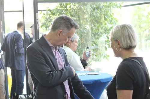 Drei Personen stehen im Foyer und unterhalten sich bei Kaffee, im Hintergrund ein ‚Ingenieur...‘